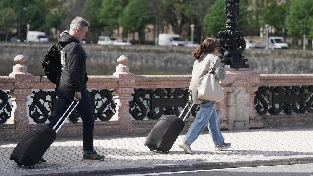 Dos turistas caminan con su maleta por el Puente de María Cristina de Donostia.