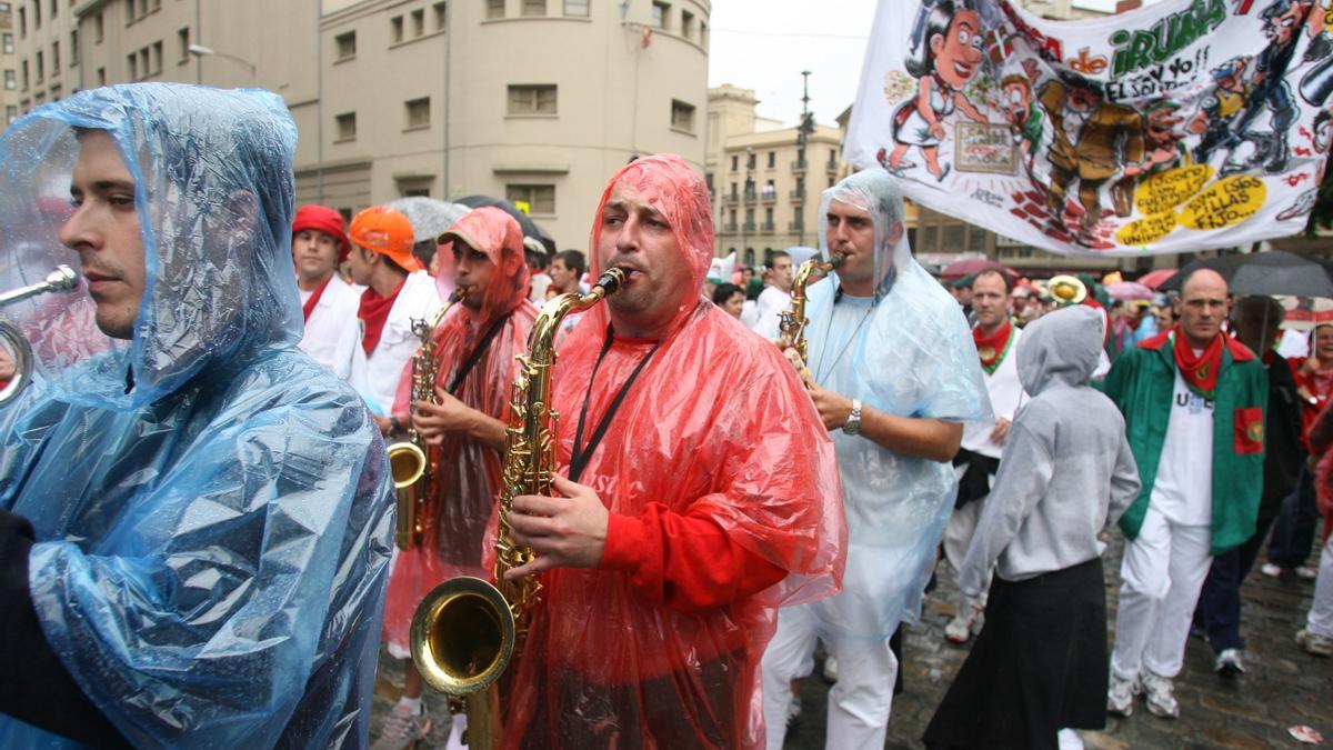 Mozos de una peña dirigiéndose a la plaza de toros cubiertos por chubasqueros para protegerse de la lluvia.