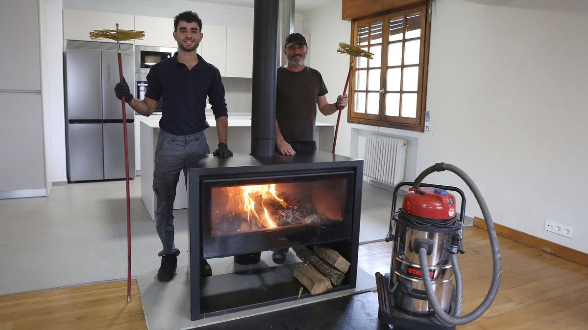 Iker Iriarte y su padre Javier, junto a una chimenea con sus herramientas de trabajo; varillas flexibles con un erizo y aspirador para recoger el hollín.