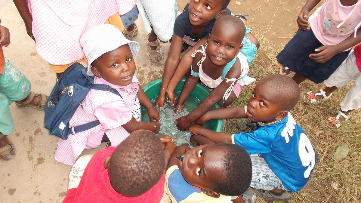 Un grupo de niños lavandose las manos en un balde de agua.