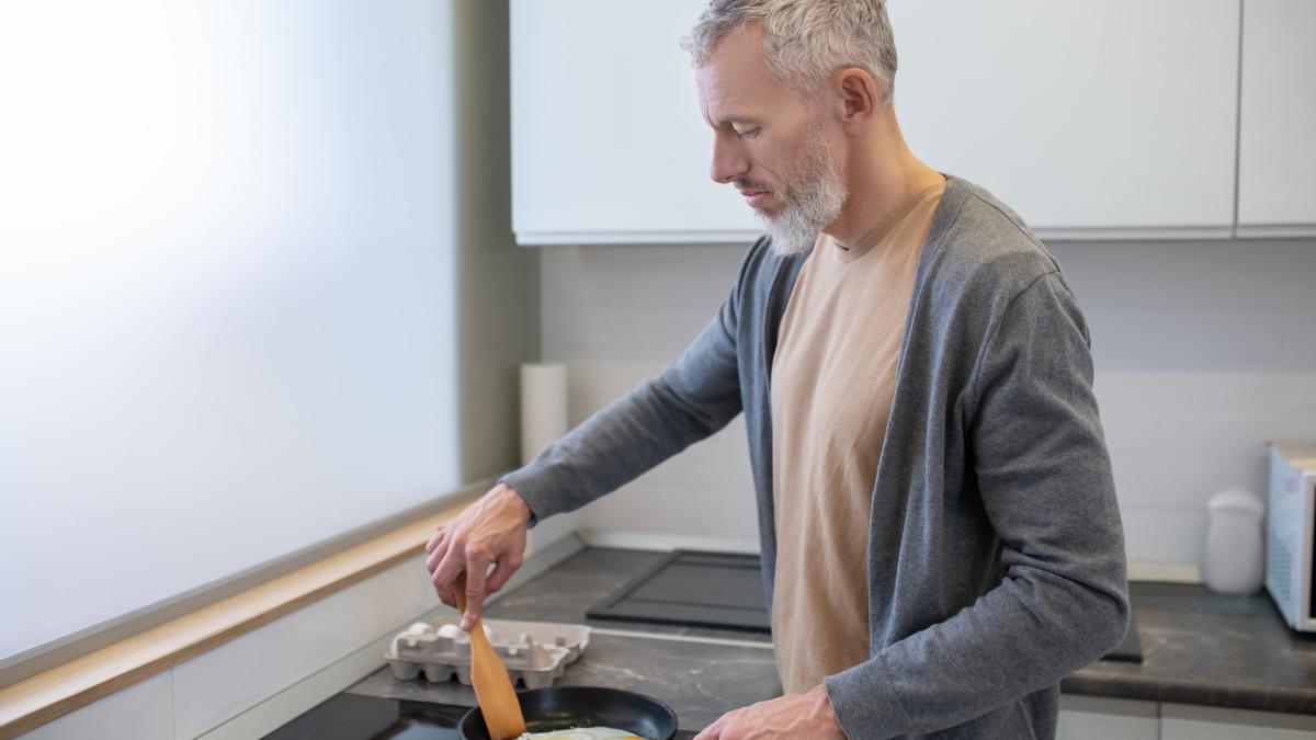 Un hombre cocina huevos fritos en una placa vitrocerámica