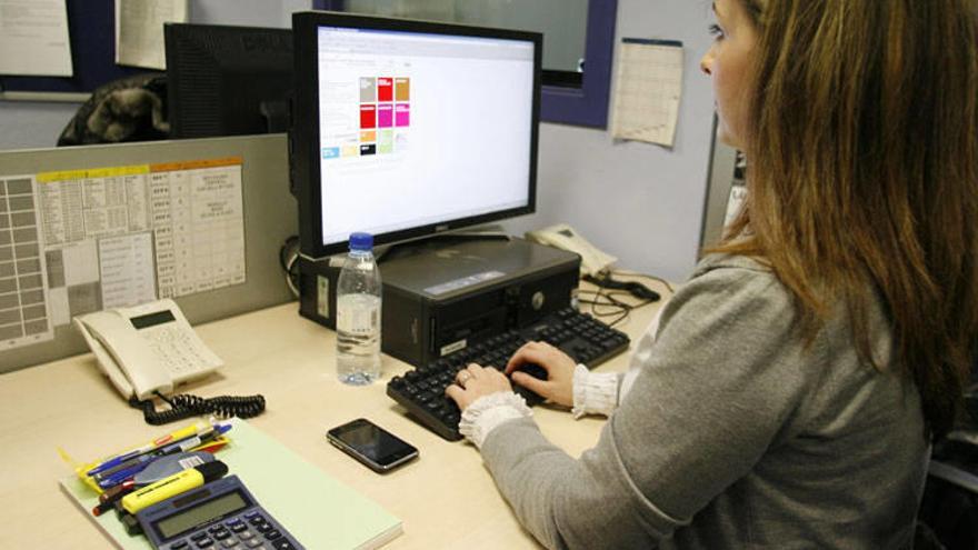 Una teletrabajadora, con las herramientas básicas para desarrollar su labor, ordenador con conexión a Internet y teléfonos.