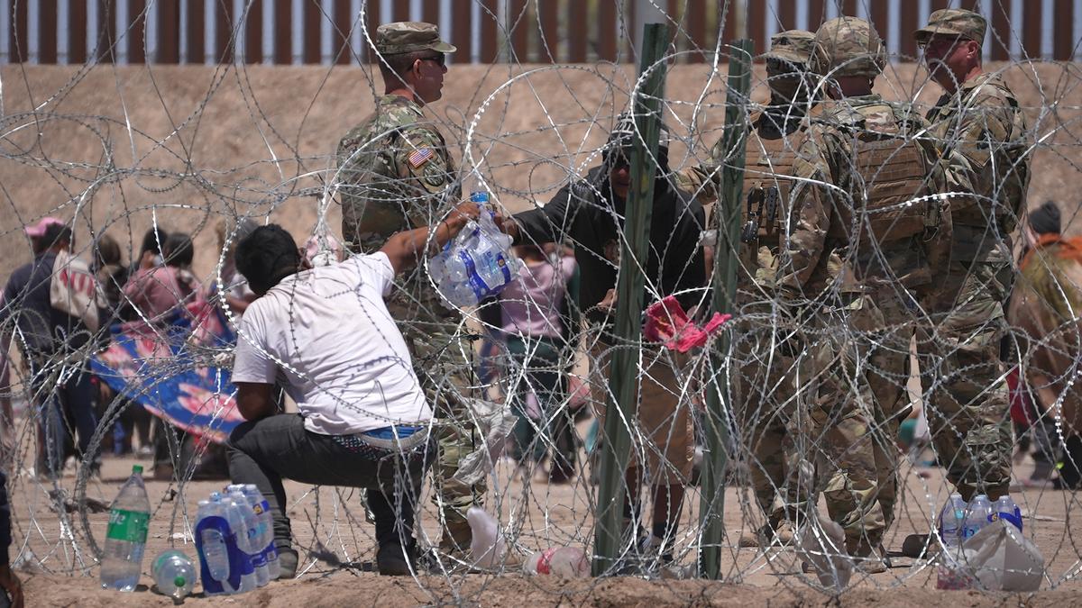 Un migrante atrapado en la frontera de Estados Unidos con México frente a un grupo de soldados americanos.