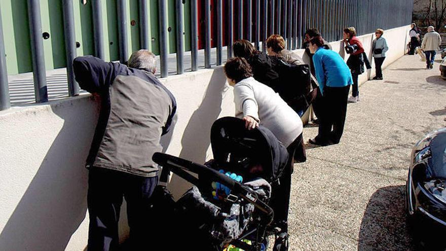 Varios familiares de los menores miran a través de los barrotes. Al fondo, la ambulancia.