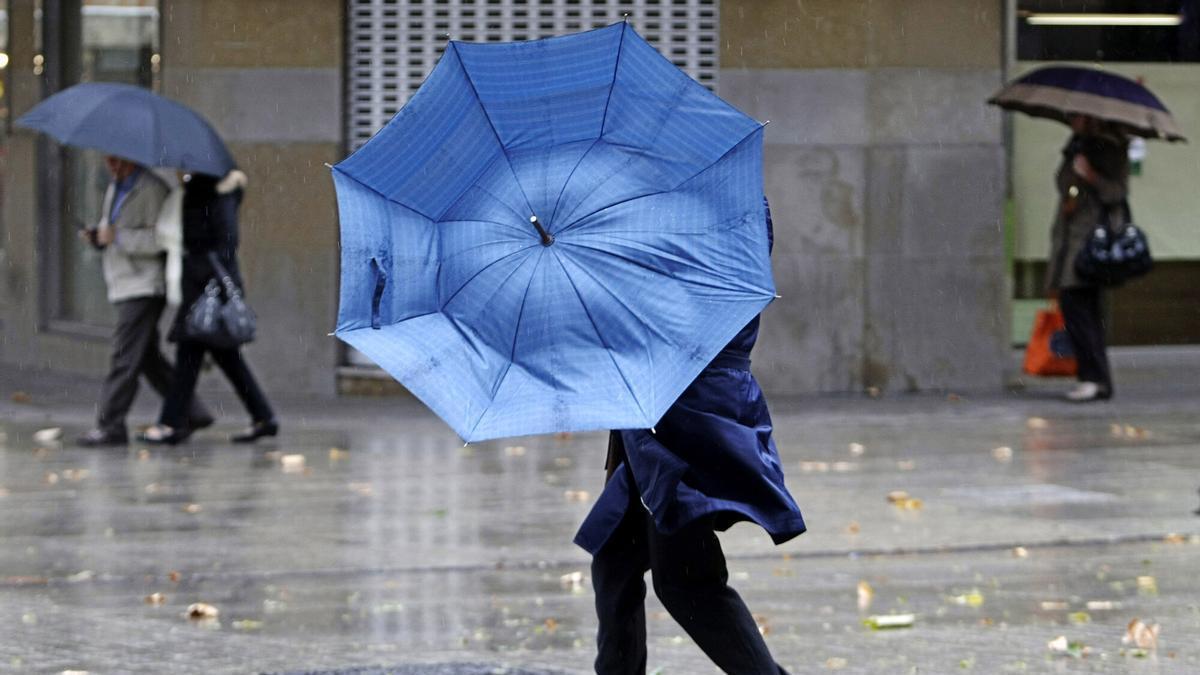 Una persona intenta protegerse del viento y la lluvia en Pamplona