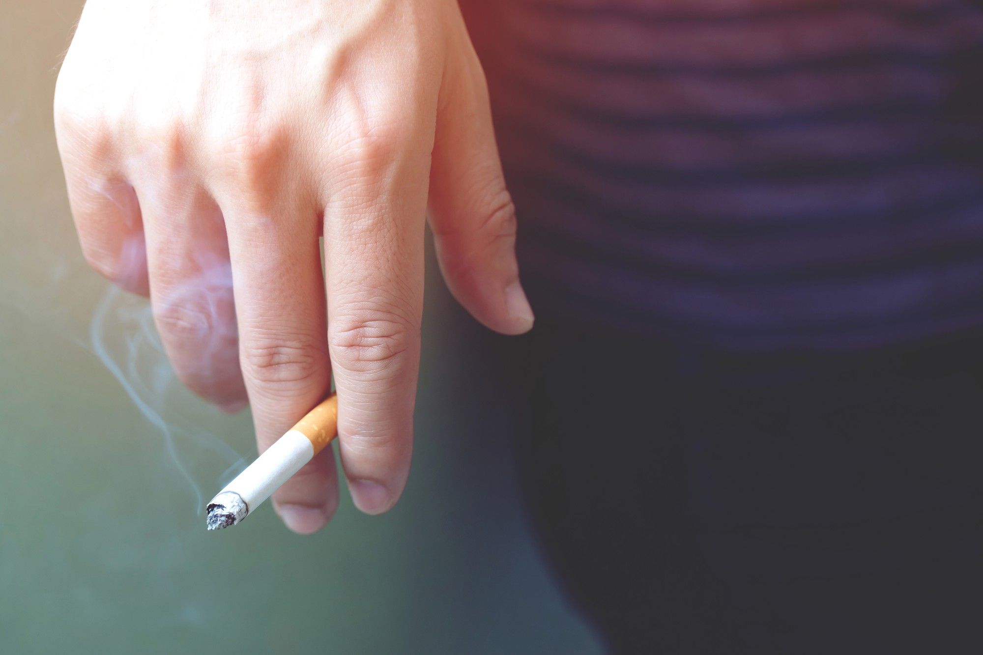 Una mano sostiene un cigarrillo encendido.
