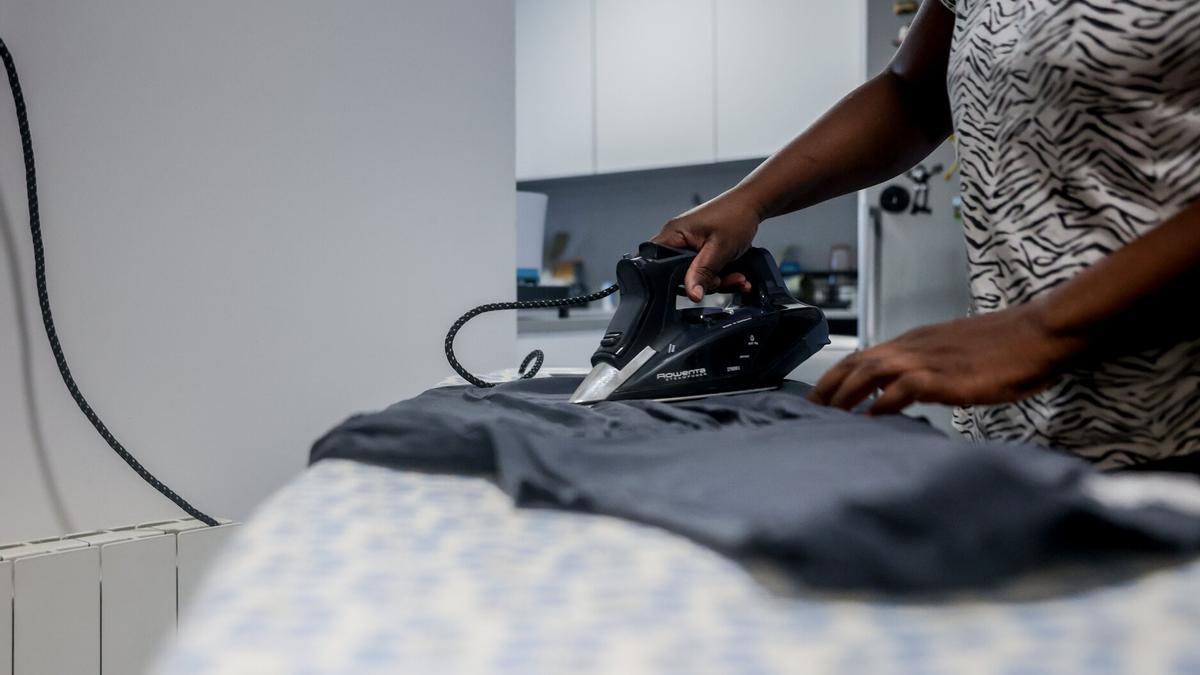 Una empleada de hogar extranjera plancha una camiseta en un domicilio donde trabaja de interna.