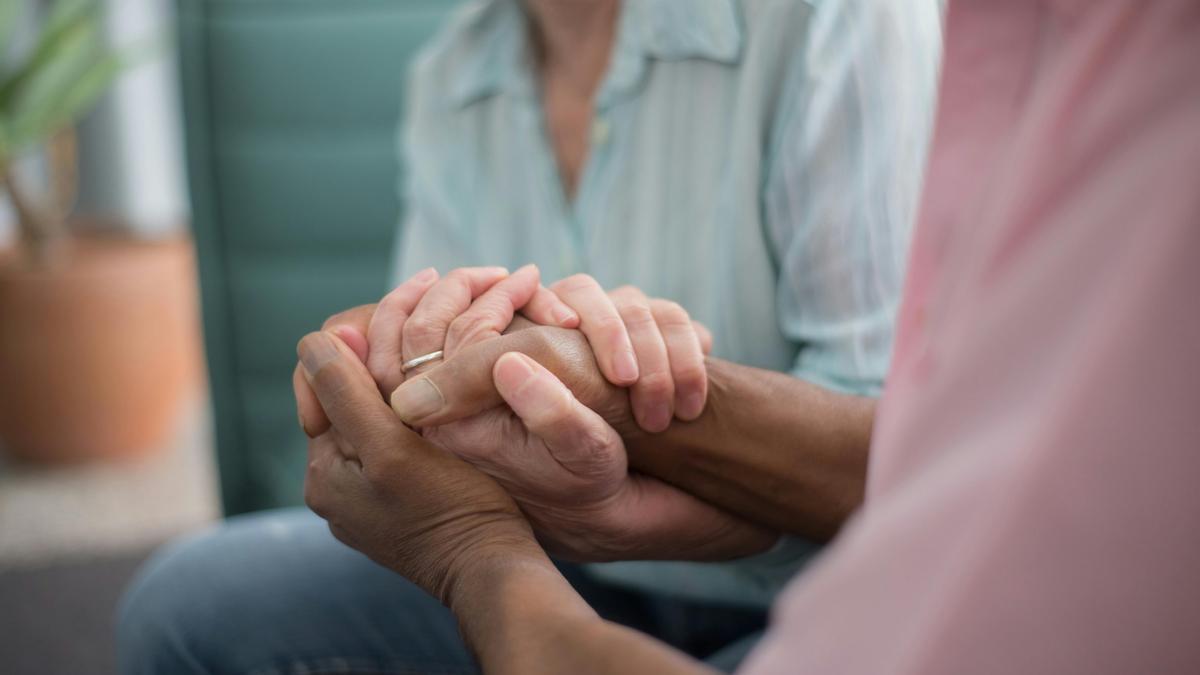 Un hombre sosteniendole la mano a una mujer mayor.