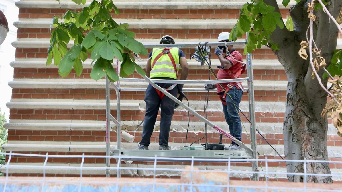Dos obreros trabajan en la fachada del centro cívico.