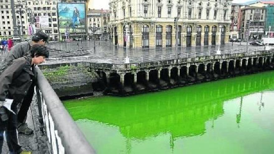 Varios transeúntes observan con asombro el intenso color verde con el que amaneció la ría de Bilbao.