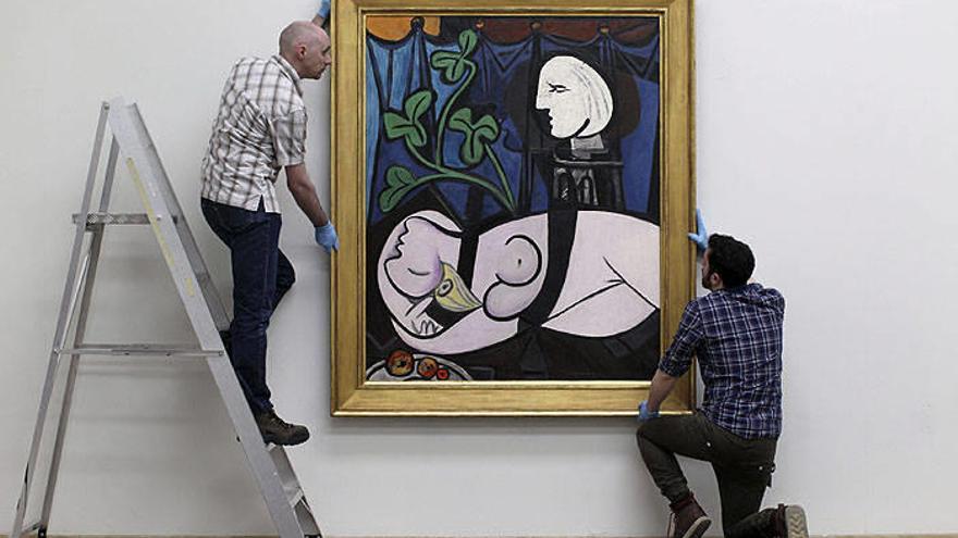 Dos operarios cuelgan el cuadro de Picasso &quot;Desnudo, hojas verdes y busto&quot;.