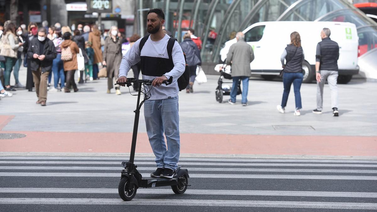Un hombre cruza la carretera por la acera en un patinete eléctrico en Bilbao.