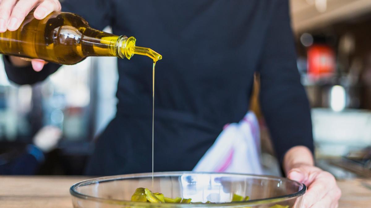 Un hombre aliña un cuenco de alubia verde con  un chorrito de aceite de oliva.