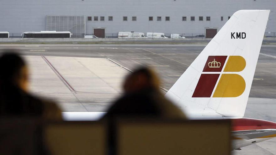 Dos personas esperan en el aeropuerto de barajas frente a un avión de Iberia.
