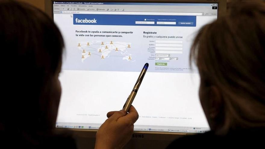 Dos jóvenes sentadas frente a la pantalla de un ordenador se disponen a crear un perfil de usuario en la red social Facebook.
