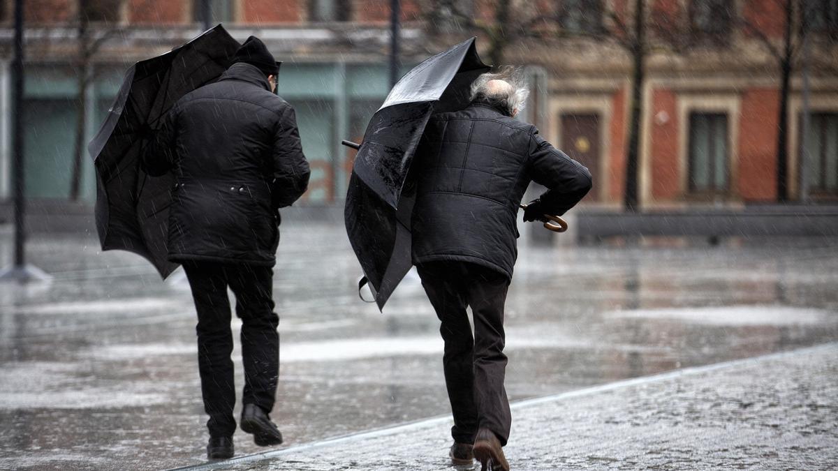 Imagen de archivo de varias personas que tratan de protegerse con sus paraguas del fuerte viento y la lluvia.