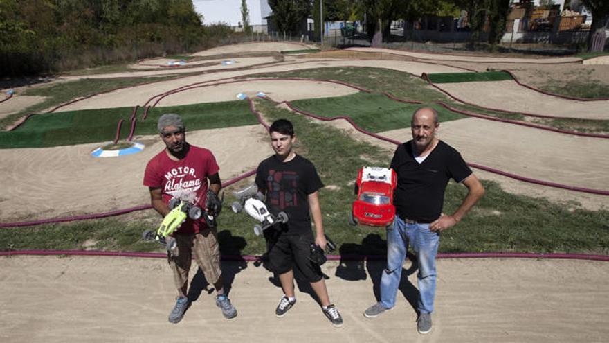 Santiago Rodríguez, Iván Ruiz y su padre, Fermín, posan con sus coches entre las manos y con el circuito de carreras de fondo.