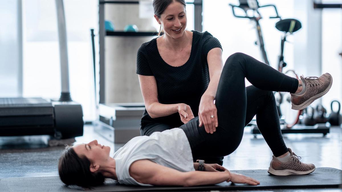 Una monitora guía a una mujer para realizar ejercicios lumbares