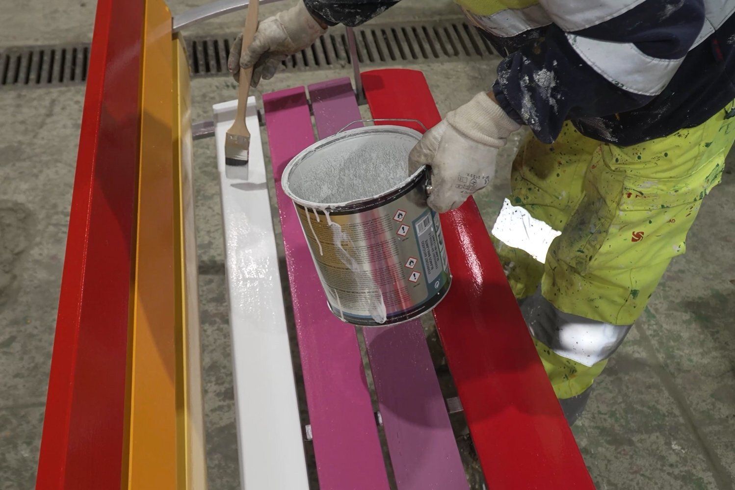 Un empleado municipal pinta un banco con los colores del arcoíris.