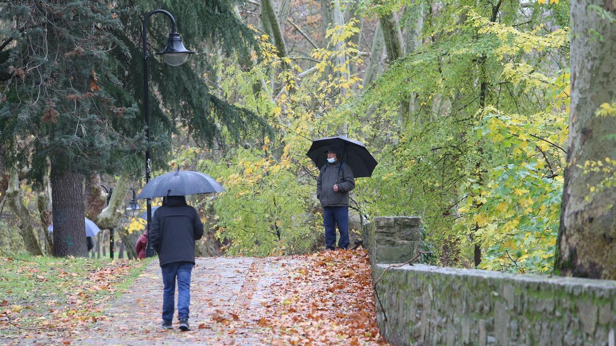 Varias personas pasean bajo la lluvia por el parque fluvial del Arga en un día otoñal.