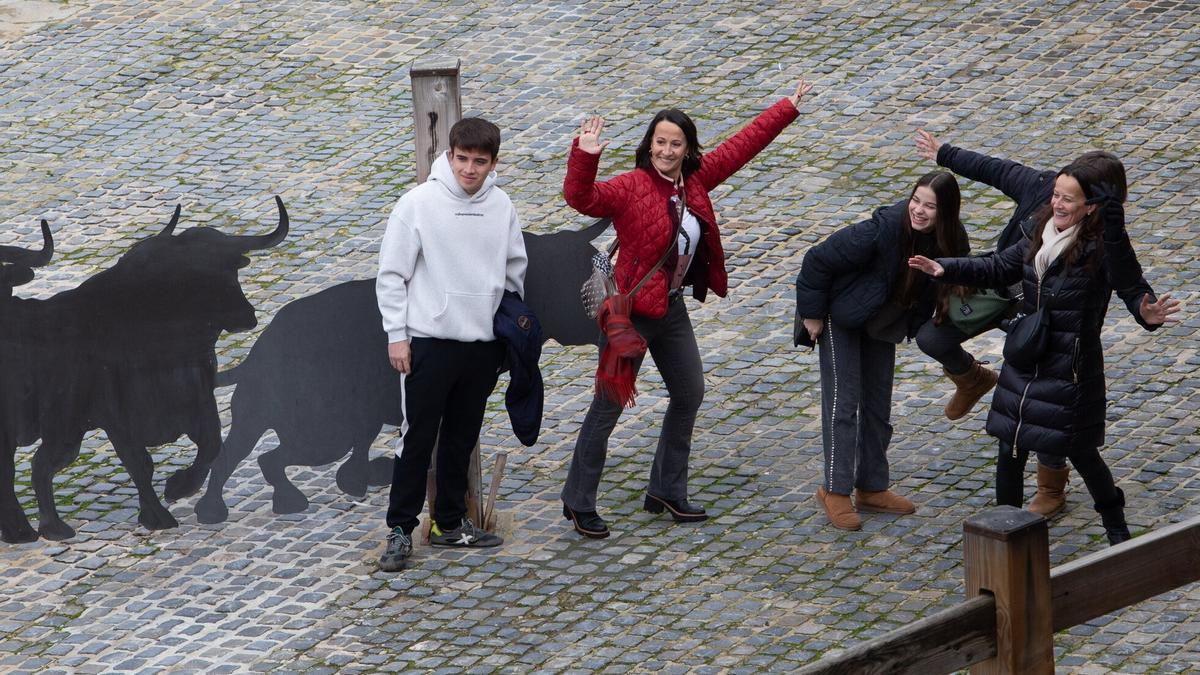 Cuatro turistas posan junto a los toros de metal en los corralillos.