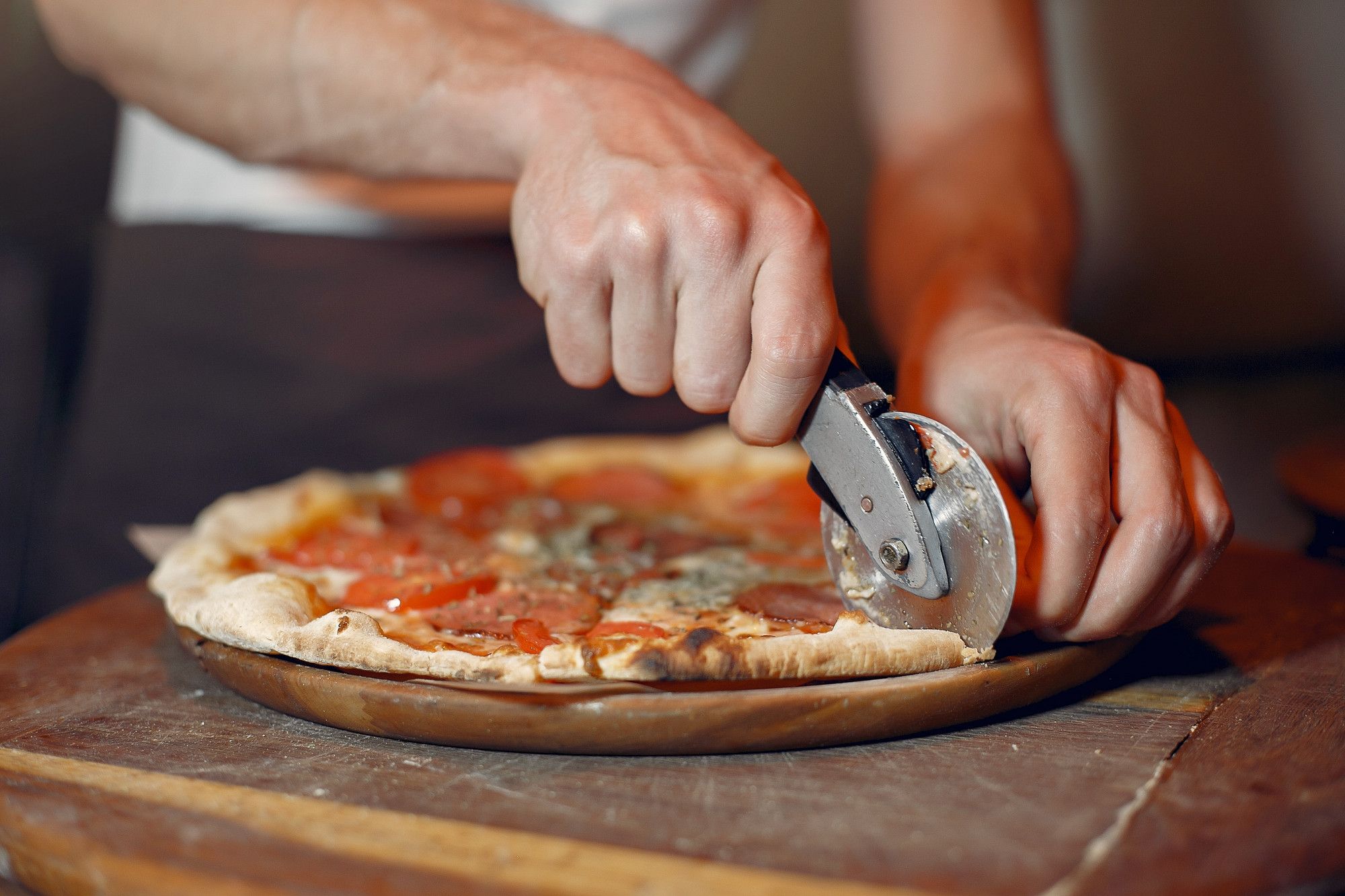 Una persona corta una pizza con un cortador de rueda.