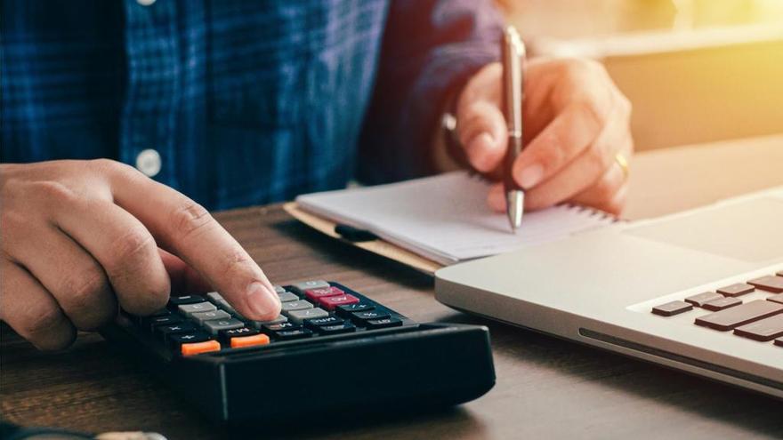 Un hombre hace cuentas con una calculadora junto a su ordenador.