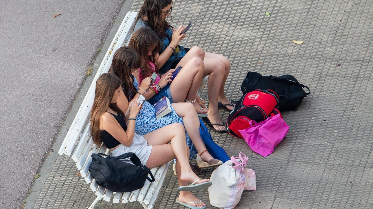 Cuatro jóvenes en un banco mirando sus teléfonos móviles.