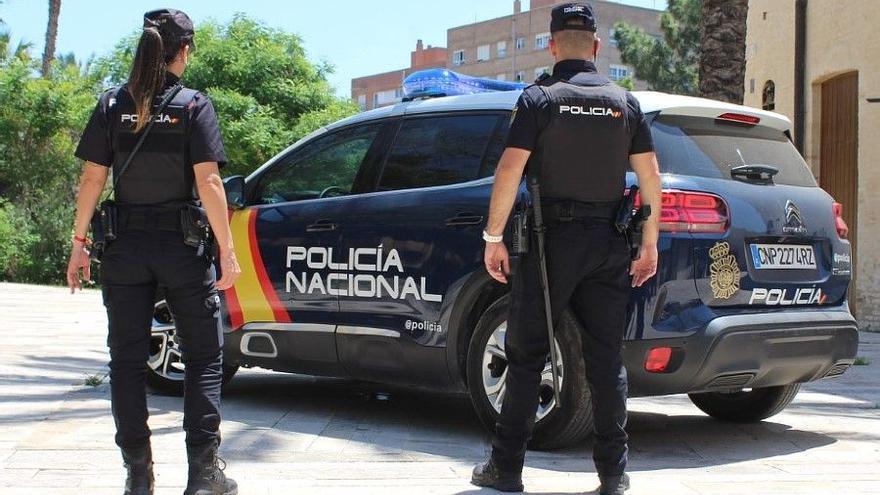 Dos agentes de la Policía Nacional uniformados junto a un vehículo policial