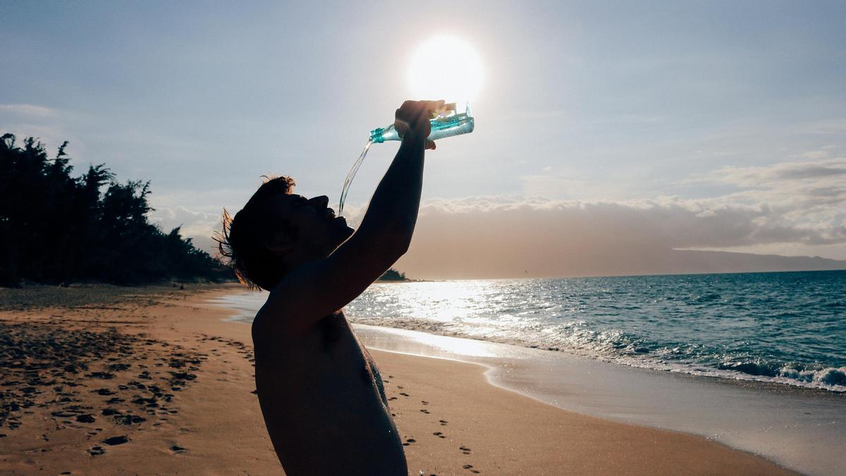 Un hombre se hidrata bebiendo agua en la playa