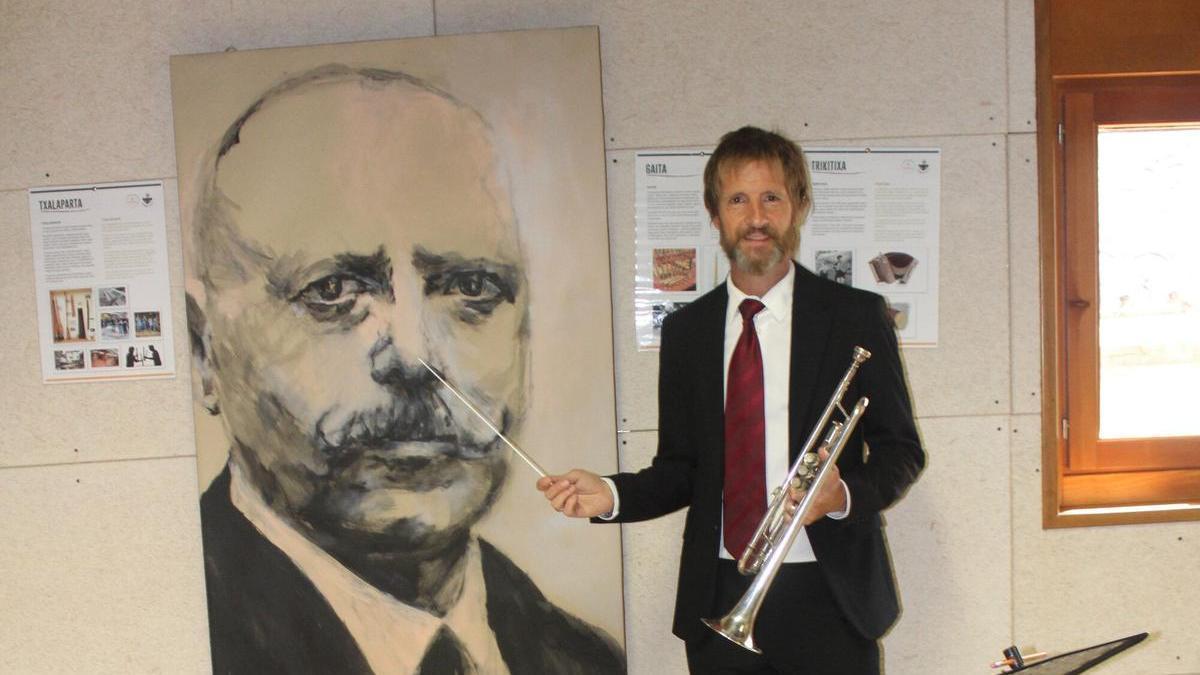 Daniel Aristu ,batuta y trompeta en mano, posa junto al cuadro del pianista Joaquín Larregla (obra de Iruña Cormenzana) que da nombre a la escuela.