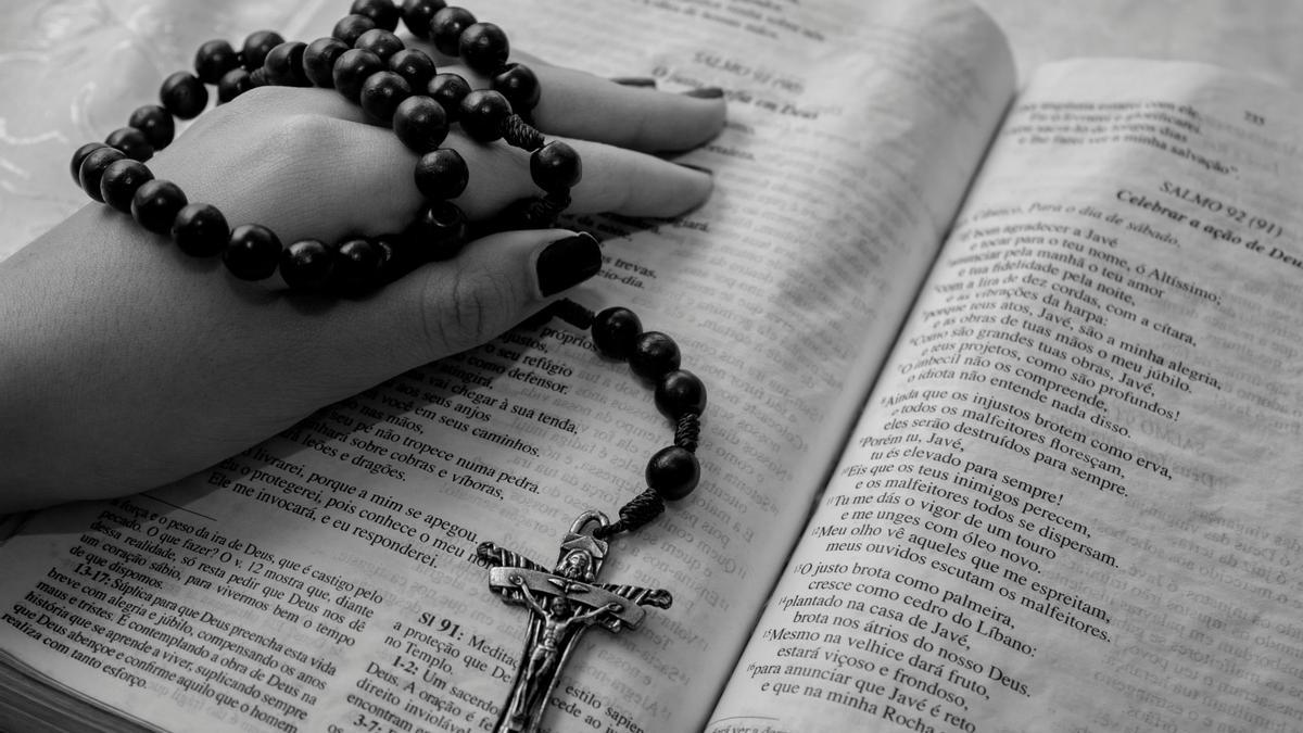 Mano sosteniendo un rosario sobre una biblia abierta.
