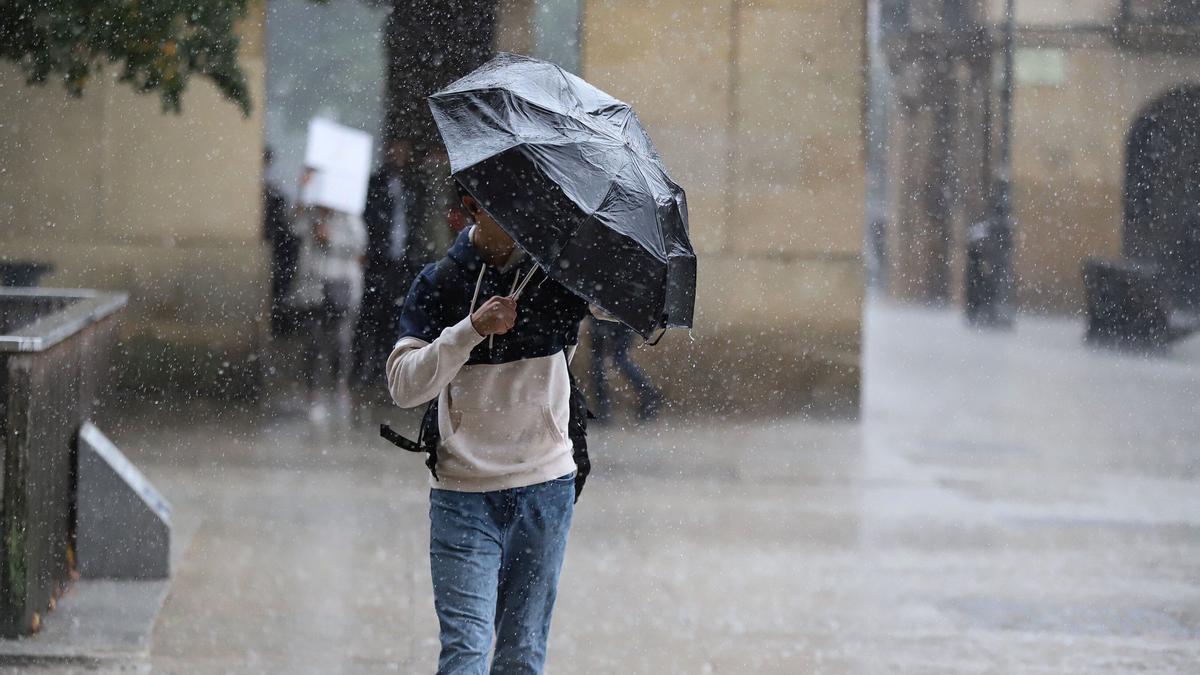 Un hombre intenta protegerse con el paraguas de la lluvia y el fuerte viento en Pamplona.