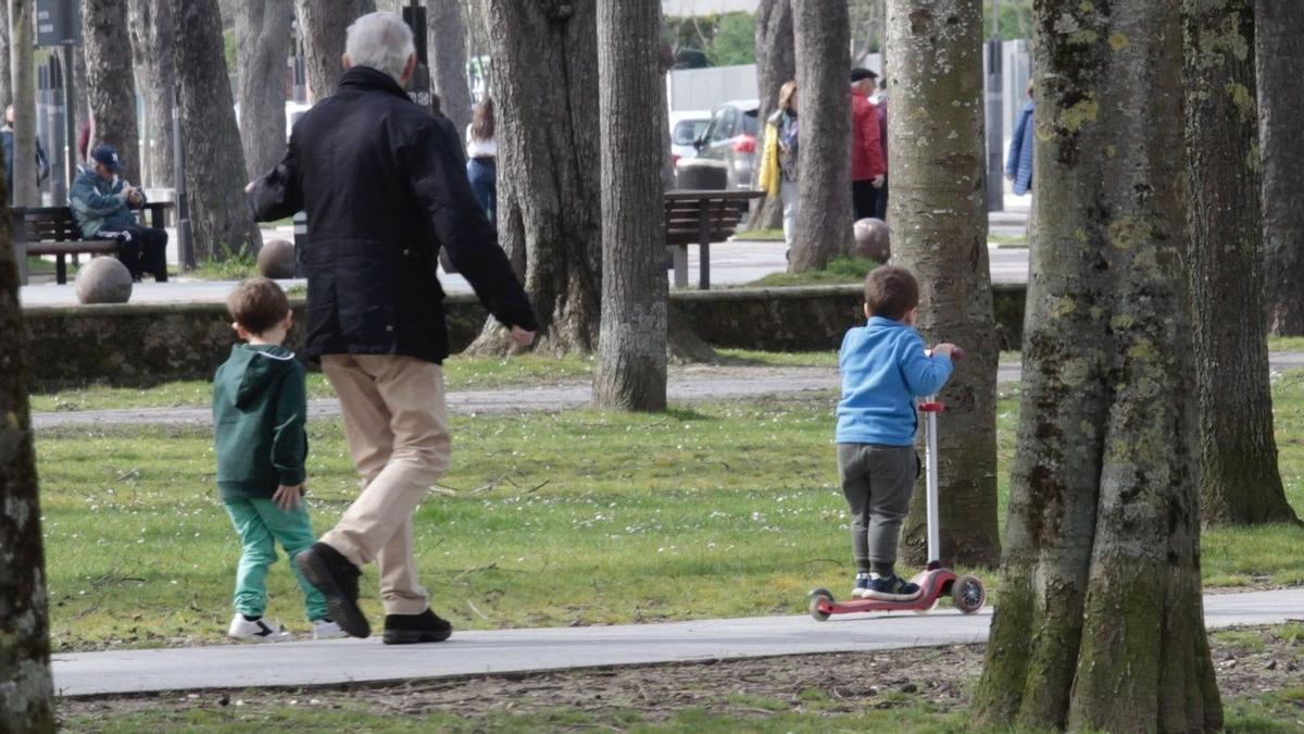 Un abuelo con sus nietos paseando por un parque.