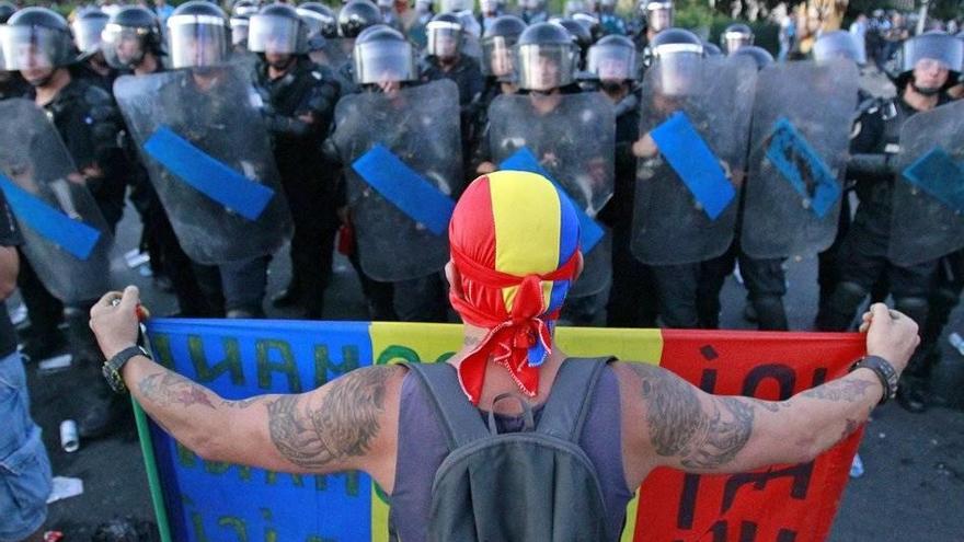 Un manifestante se enfrenta a la Policía antidisturbios con la bandera de Rumanía en la capital, Bucarest.