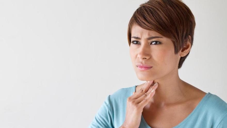 Una mujer con expresión de dolor se toca la garganta.