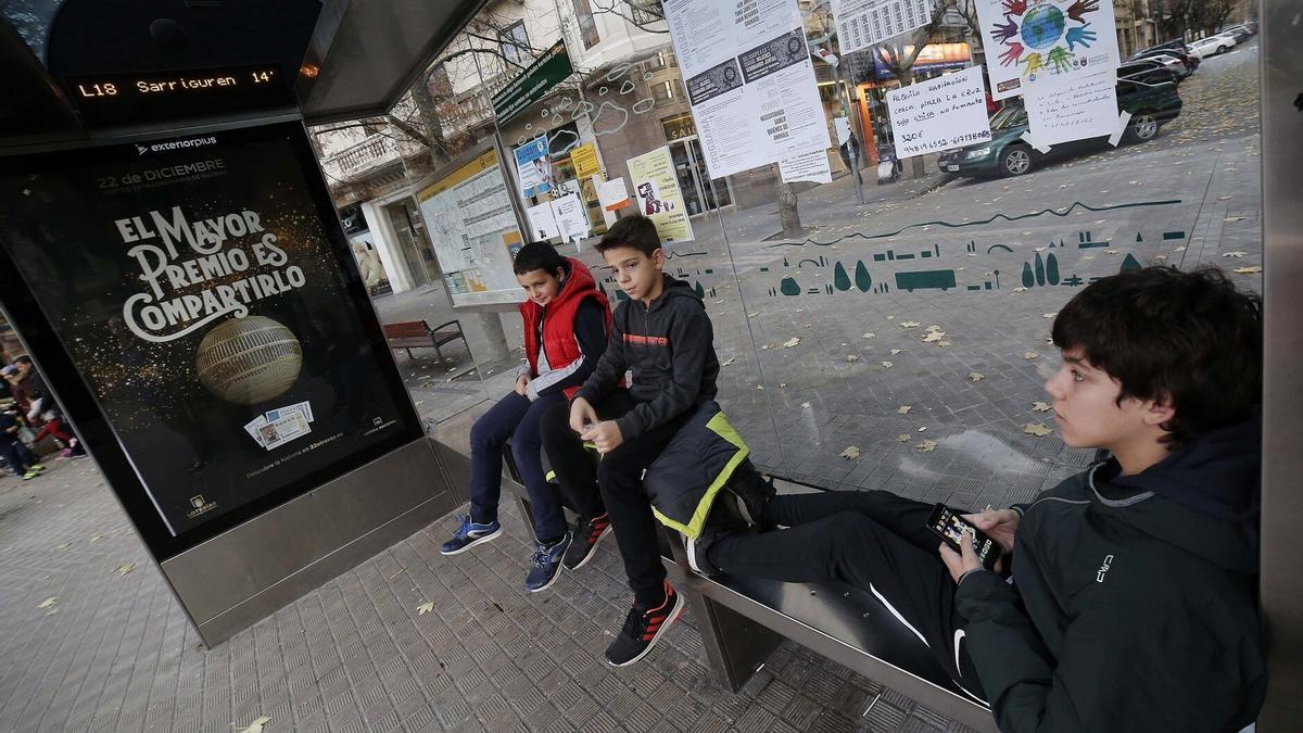 Tres niños esperan en la parada de Príncipe de Viana la llegada de la villavesa.