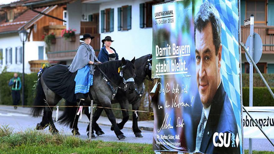 Participantes del tradicional festival Sankt Coloman cabalgan junto a un cartel electoral del CSU, el partido ganador de estos comicios, que ha perdido su mayoría absoluta.Foto: Afp
