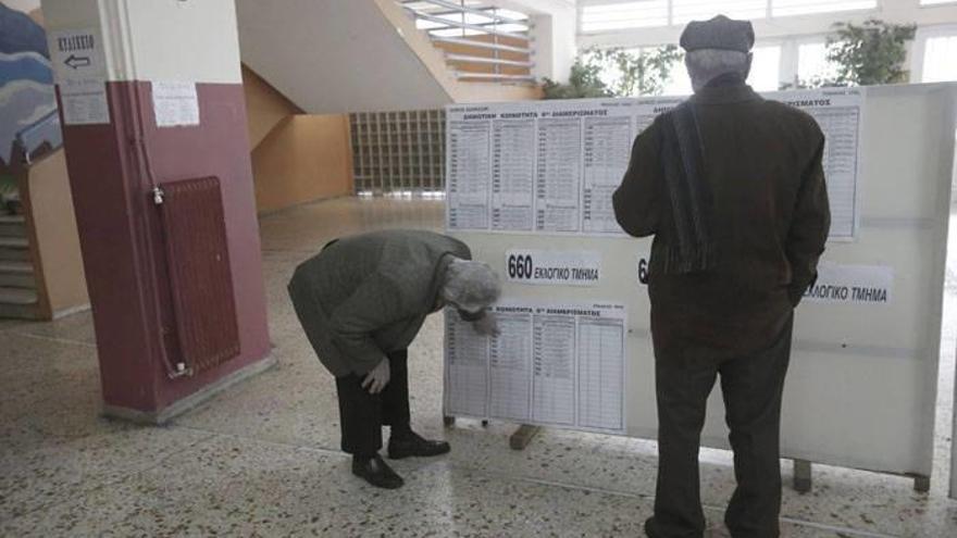 Dos hombres observan un panel informativo en un colegio electoral.