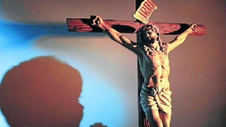 Sombra de un niño rezando ante una figura de Jesucristo crucificado.