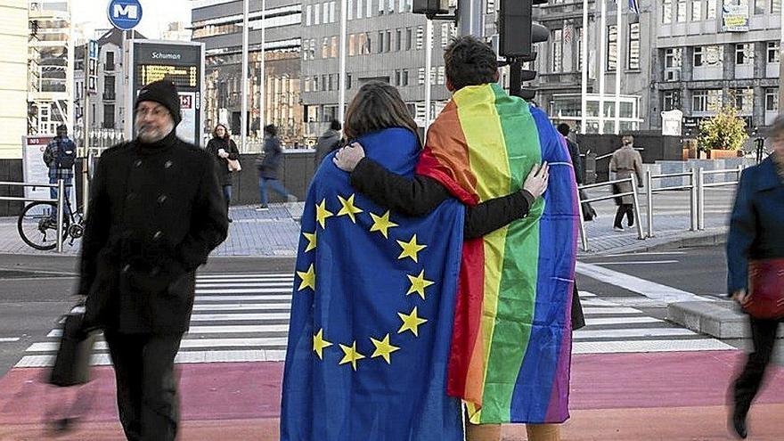 Una pareja, con una bandera de la UE y una LGTBIQ, se abraza. Foto: Efe