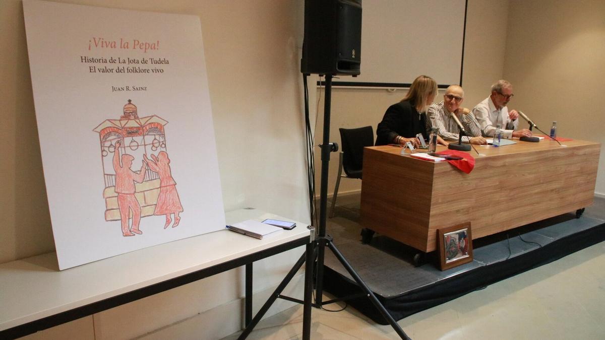 Portada del libro durante la presentación, Juan Sáinz en medio de la mesa con la concejala Les y Javier Munáriz.