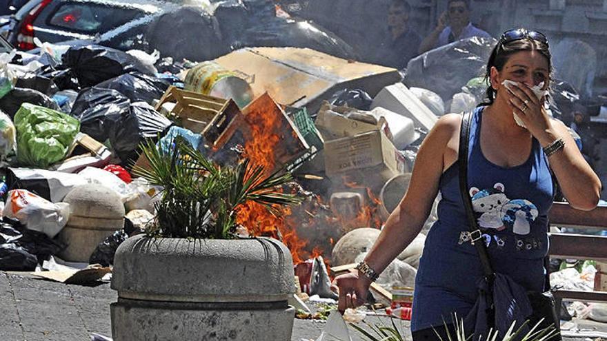 Una mujer camina junto a una montaña de basura en llamas en una calle de Nápoles, Italia.