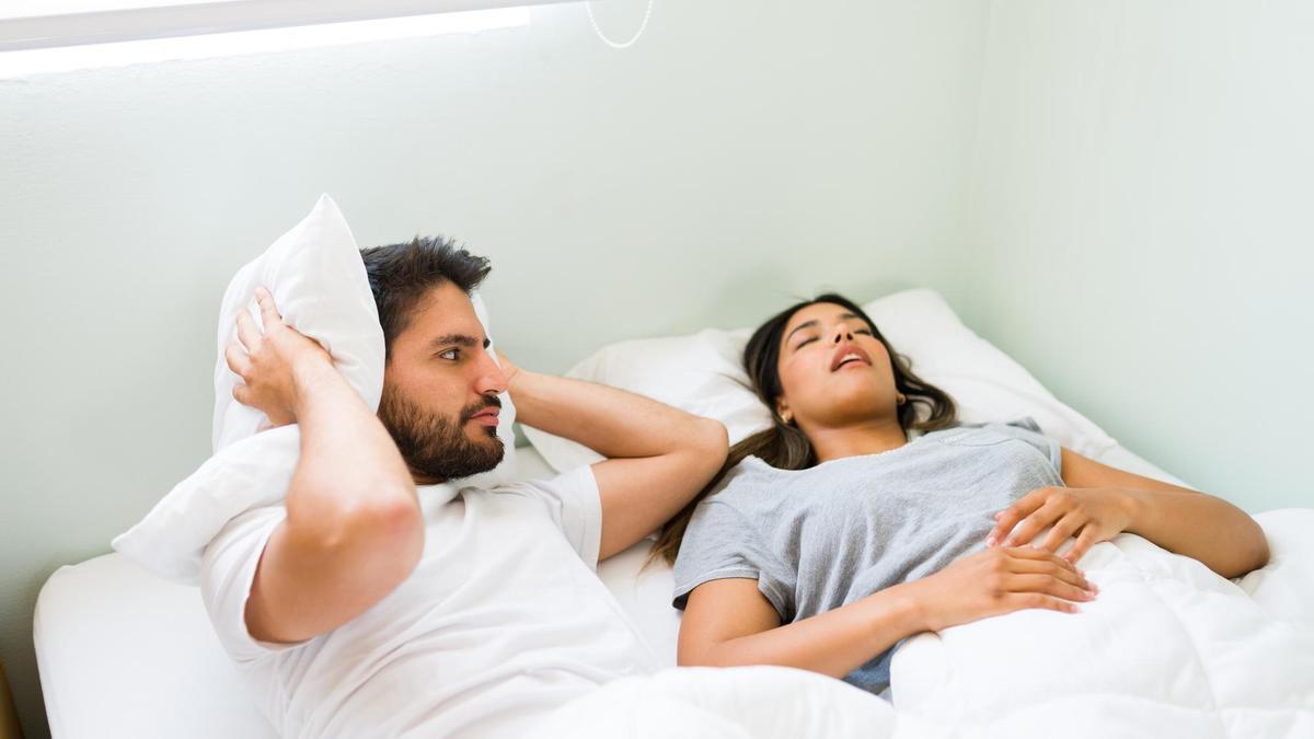 Un hombre se tapa los oídos con la almohada mientras su pareja ronca.