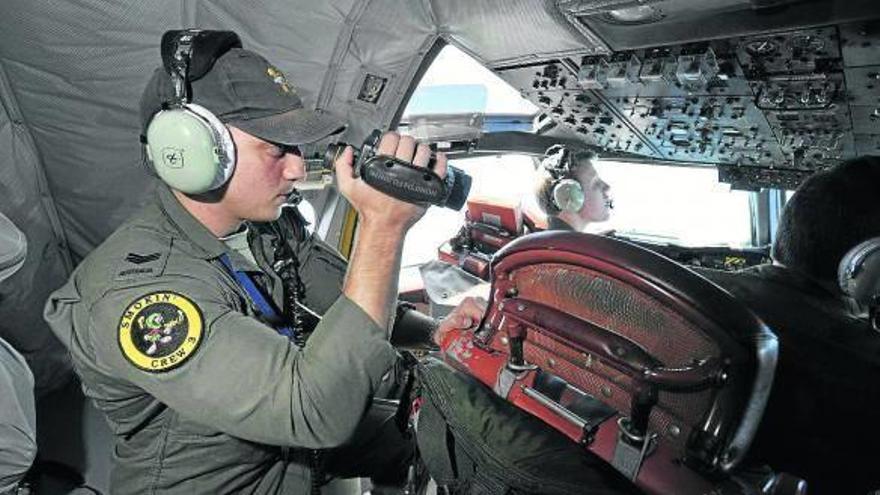 Un soldado australiano mira con unos prismáticos desde un avión hacia el mar.