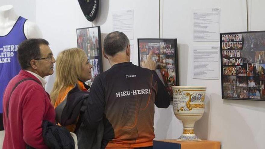 Personas viendo la exposición fotográfica con motivo de la celebración del 25 aniversario del Club Hiru Herri en la Casa de Cultura de Burlada.